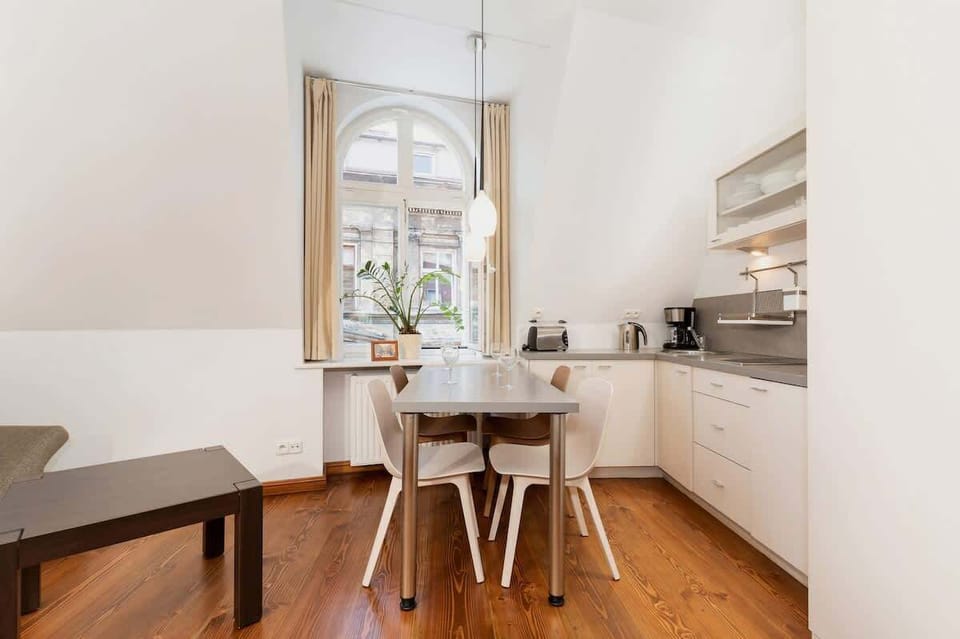 A different view of the open-plan kitchen and dining area. The table is surrounded by white chairs, and there’s plenty of natural light coming in from the windows.

