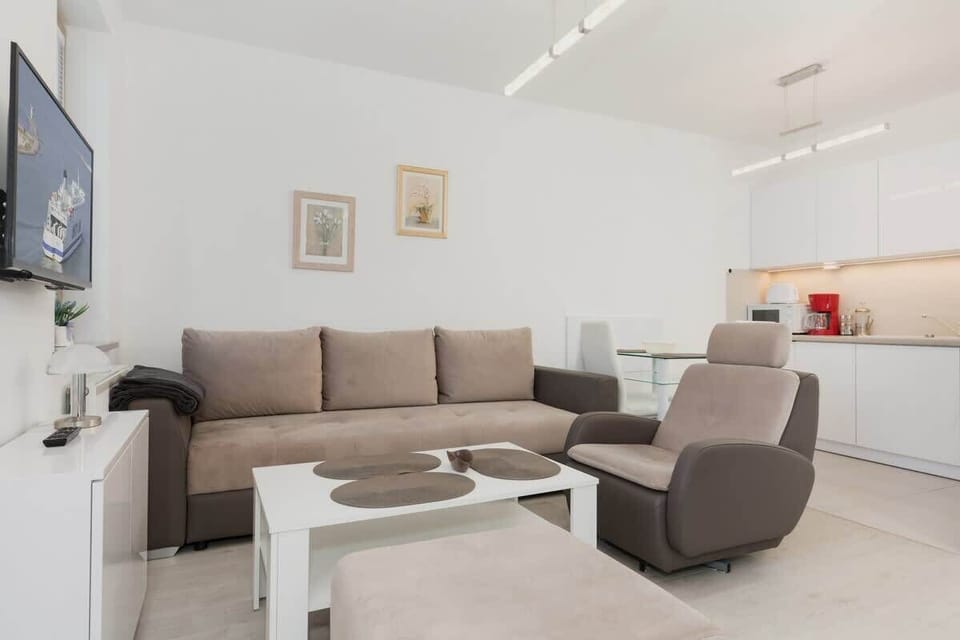Cosy and elegant living room with stylish sofa bed, armchair, television, and white kitchenette.