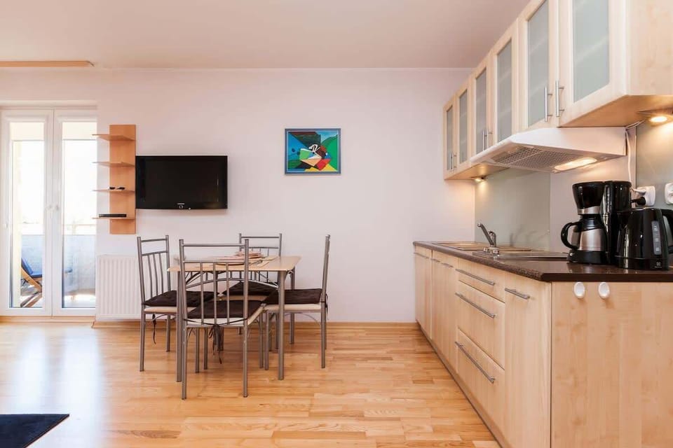 Another shot of the living room, this time seen from a different angle. Part of the kitchen is in the background, and the dining table with four chairs is visible in the foreground. The interior decoration is bright and modern.