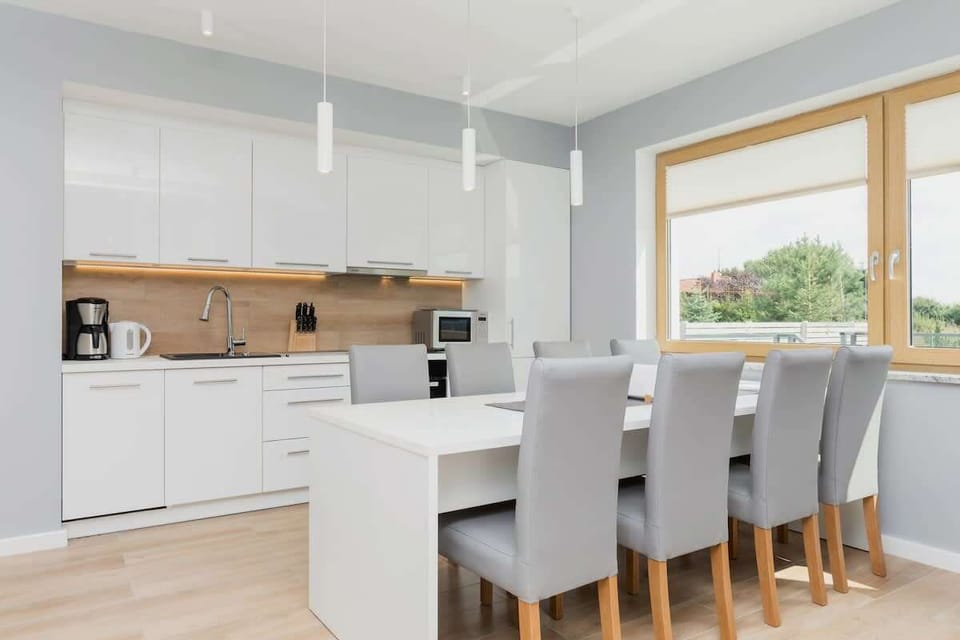 A stylish kitchen with white cabinetry and wood countertops, leading into an open-plan living area with elegant decor and modern lighting.