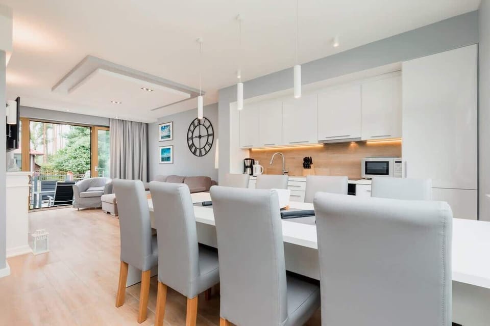 A stylish kitchen with white cabinetry and wood countertops, leading into an open-plan living area with elegant decor and modern lighting.