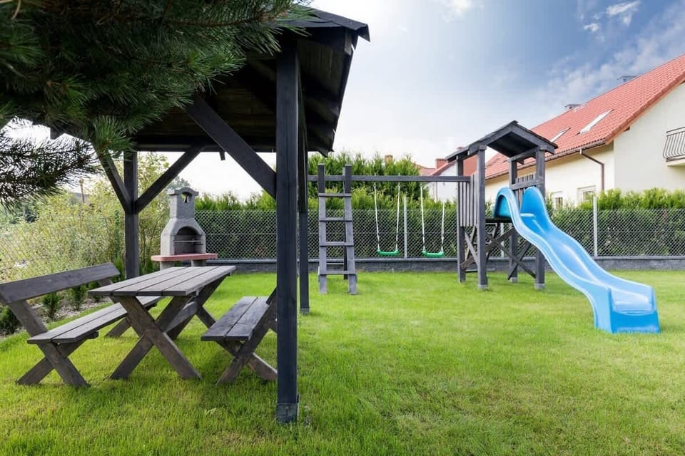 The backyard of a modern house, featuring a neatly maintained garden, a play area with swings, and outdoor seating under a wooden gazebo, perfect for family gatherings.