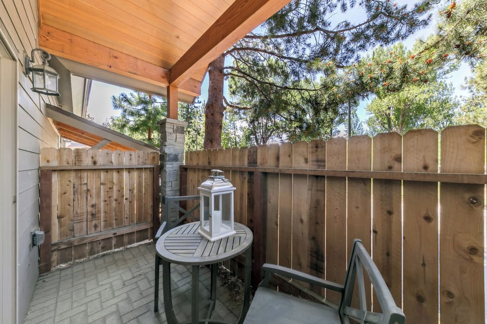 Your private patio offers a peaceful retreat with warm wood accents, a cozy table for morning coffee, and mature trees creating natural shade overhead.