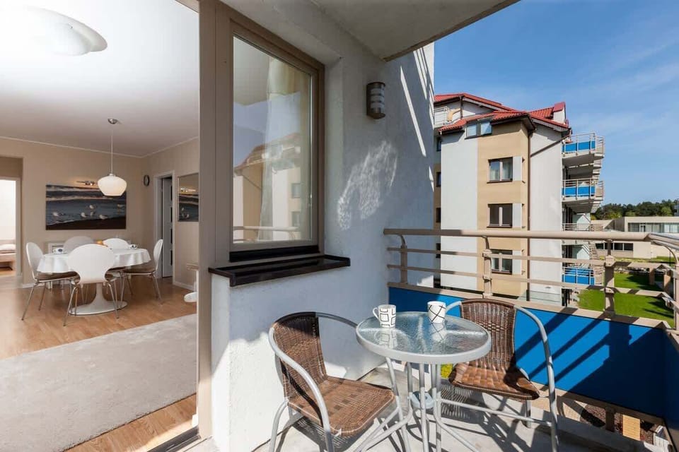 A cozy balcony with blue chairs and a small table, offering a view of a well-maintained residential complex. The balcony overlooks a green area, perfect for relaxation.