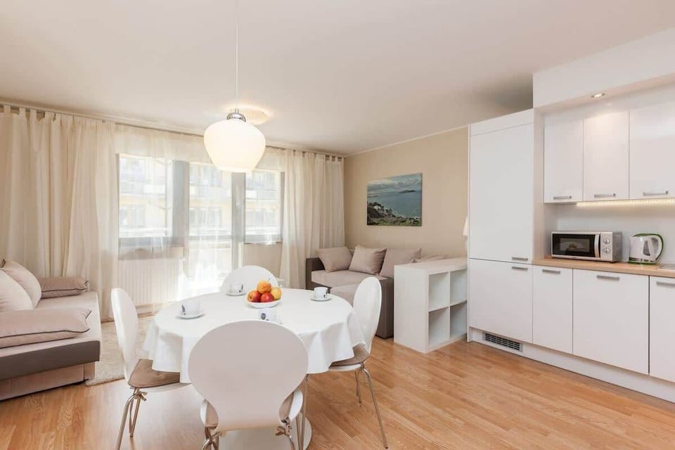A modern living room with a comfortable sofa, a white coffee table, and a TV on a console. The space is designed to be bright and welcoming with wooden floors and neutral tones.