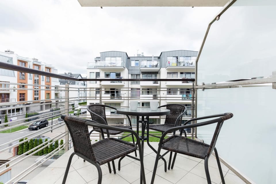 A balcony with a small table and two chairs overlooks a modern residential area with plenty of outdoor greenery. It provides a quiet spot to enjoy fresh air and relax.