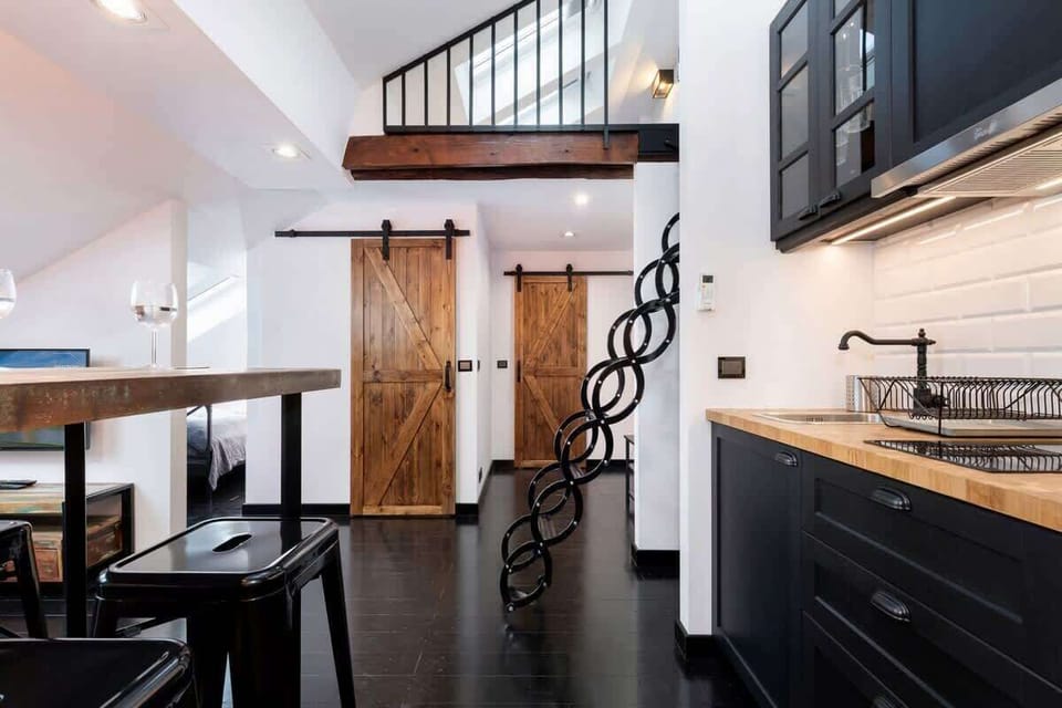 A modern kitchen with black cabinets and a dining area nearby. The setup is spacious and combines an industrial style with comfort.
