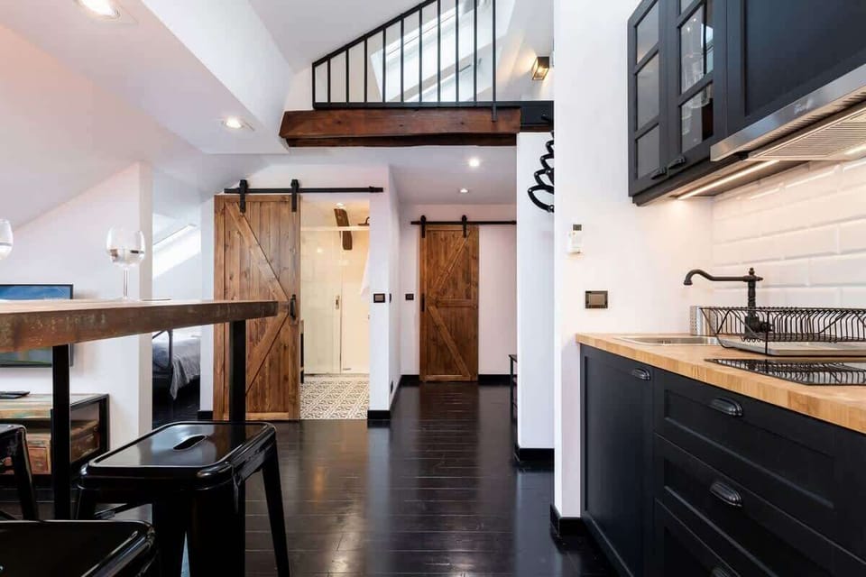 An open-concept living area with a black dining table and an exposed brick wall. The room feels expansive with its high ceilings and ample natural light.