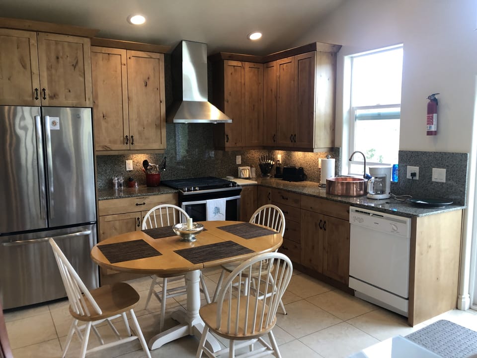 View of Hood, Full GE Refrigerator, Copper Sink, DW and Dining for 4.


