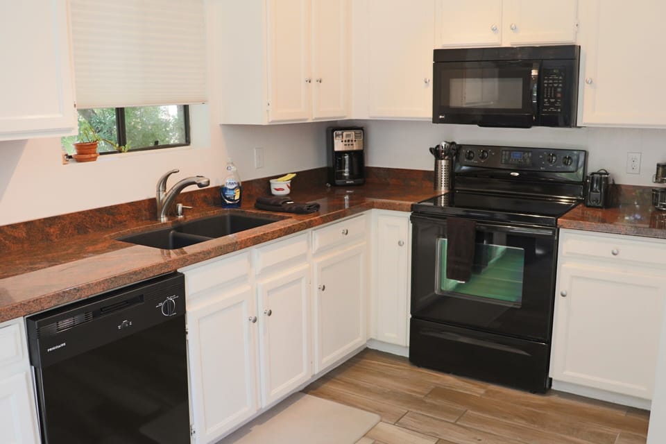 Red granite counter tops offset by white cupboards and black appliances.