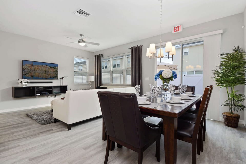 Sunny dining space with large windows, three-panel wall art, and a chic chandelier-ideal for gatherings.