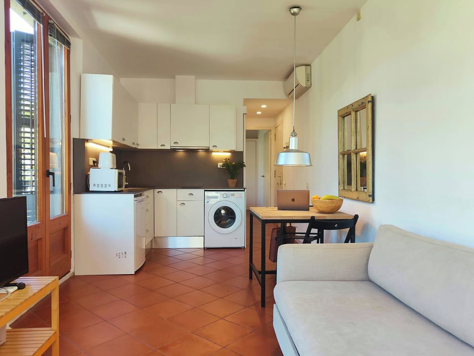 The living room features a comfortable sofa positioned in front of a wooden table. The apartment has terracotta tile floors throughout.