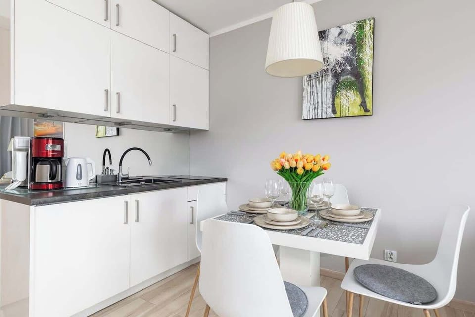 A compact but modern kitchen featuring white cabinetry, a coffee machine, and a vase with flowers.
