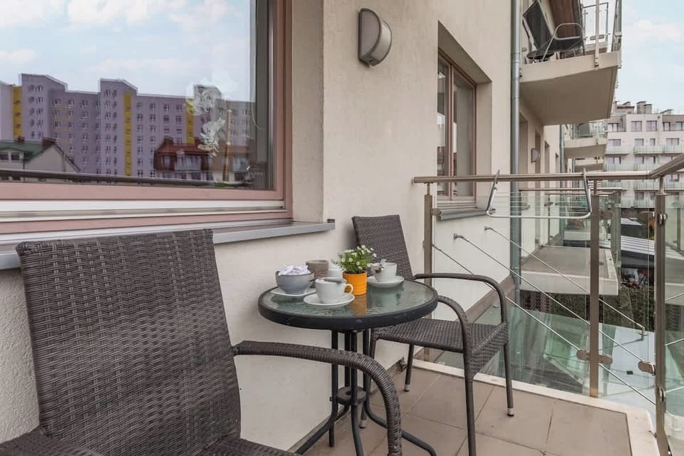 A cozy balcony with outdoor seating, overlooking the green neighborhood area.