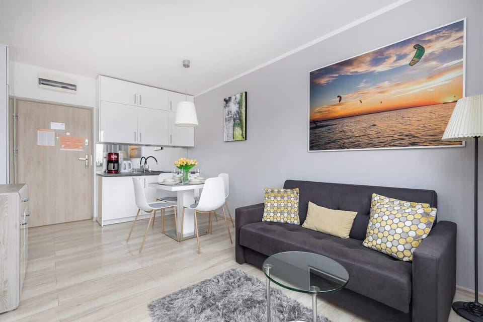 The living area with a grey sofa over which hangs a painting is coherently connected by a dining table with a kitchenette.
