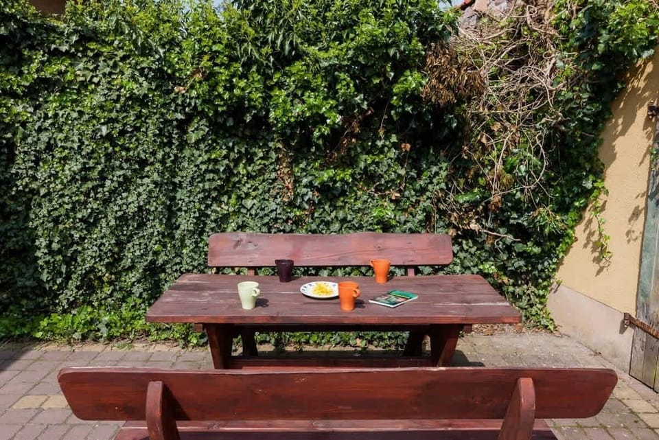 A wooden table and benches standing in front of the house. 