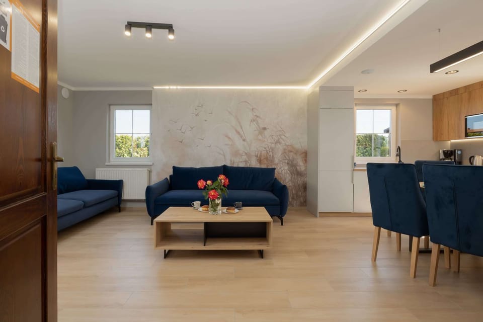 A modern living room featuring a spacious blue sectional sofa, wooden coffee table, and large windows that flood the space with natural light, creating an inviting and airy atmosphere.