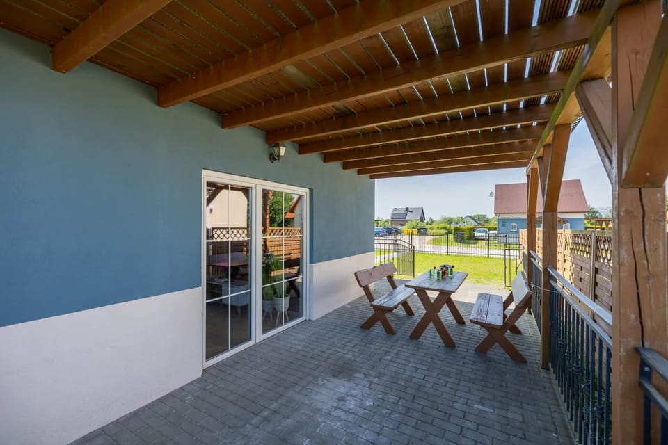 A spacious covered patio with a rustic wooden table and benches, perfect for al fresco dining and enjoying the outdoors in comfort and style.