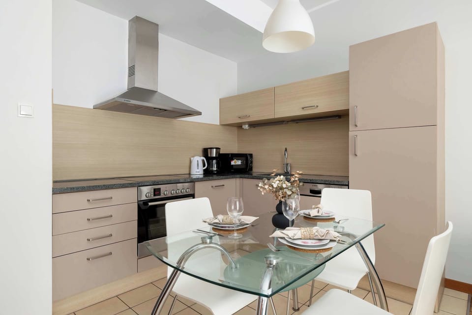 A modern kitchen corner with a glass dining table set for a meal. The design is minimal and neatly organized.