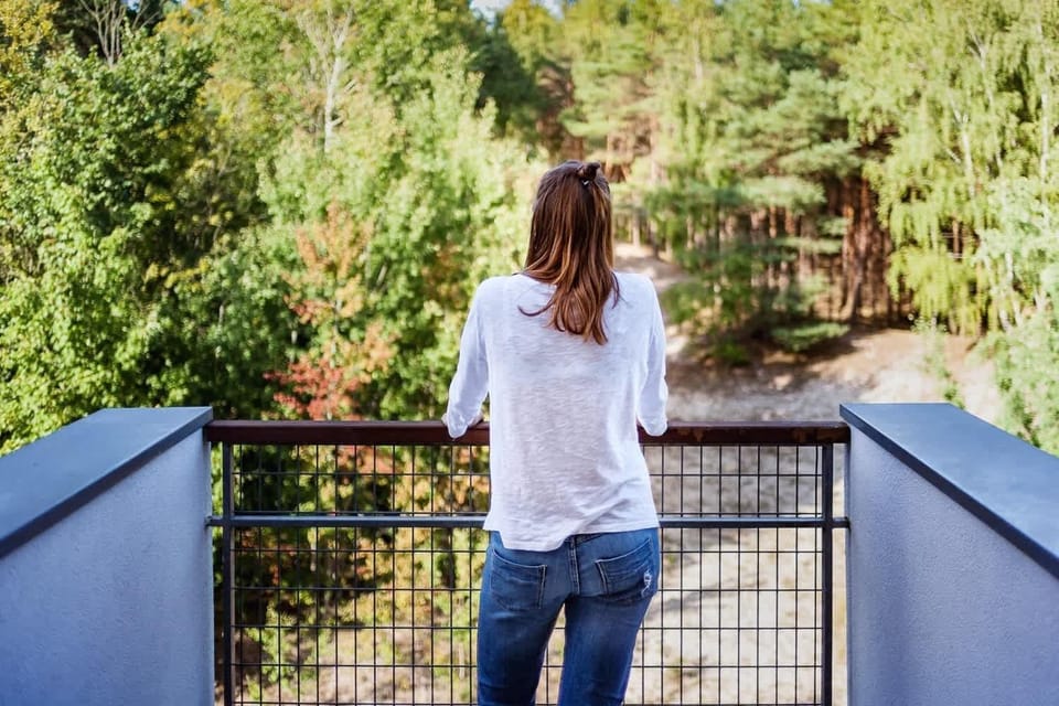  A person standing on a balcony, looking out over a lush, green landscape. The view suggests a peaceful, natural setting, ideal for relaxation.