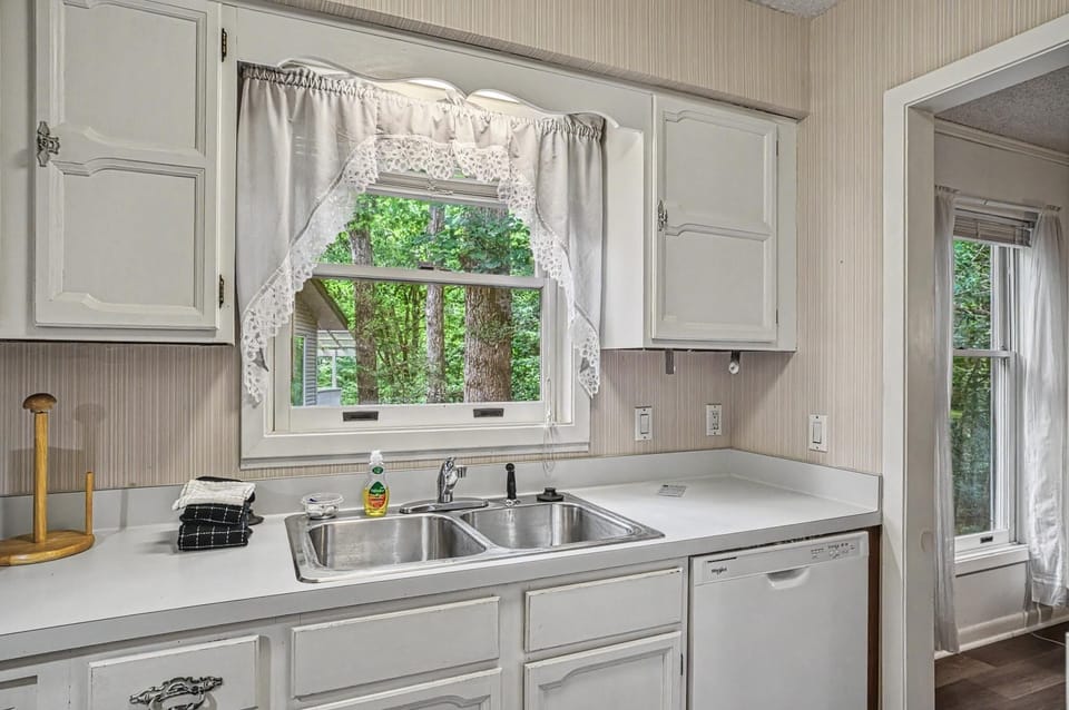 Your bright, fully-equipped kitchen overlooks lush greenery through a charming window—perfect for preparing meals while enjoying peaceful views.