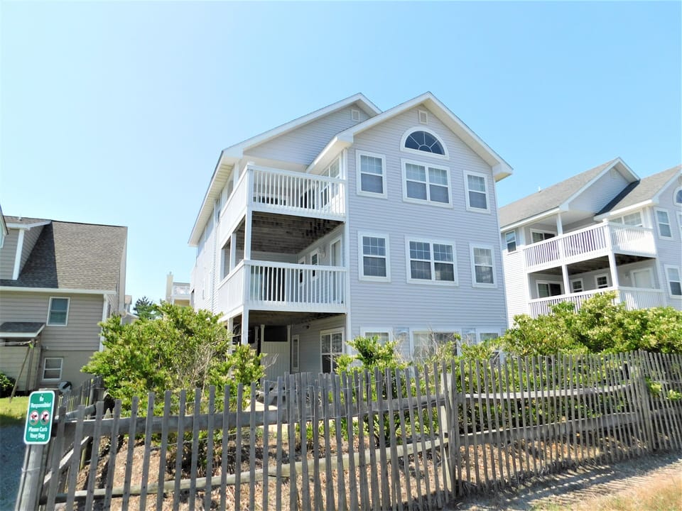 7 South Carolina Avenue - Side Exterior View - A side angle view of the multi-story beach home, showing the balconies and weathered wooden fence.
