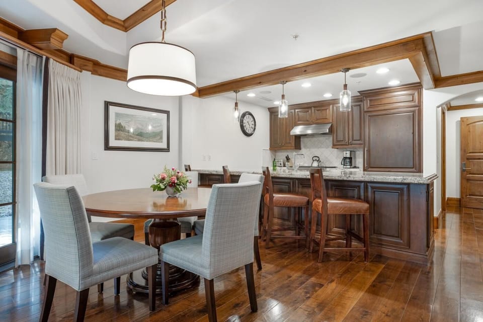 Dining area with round wood table, upholstered gray chairs, and pendant light above polished hardwood floors.