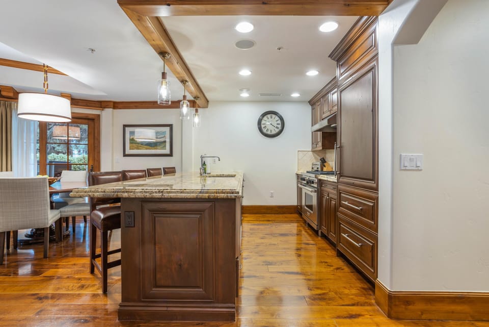 Granite-topped island with leather barstools faces dark wood cabinetry and stainless steel appliances in the kitchen.