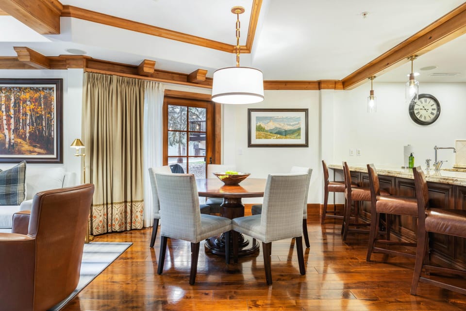 Round wood dining table surrounded by four gray upholstered chairs beneath a drum pendant light.