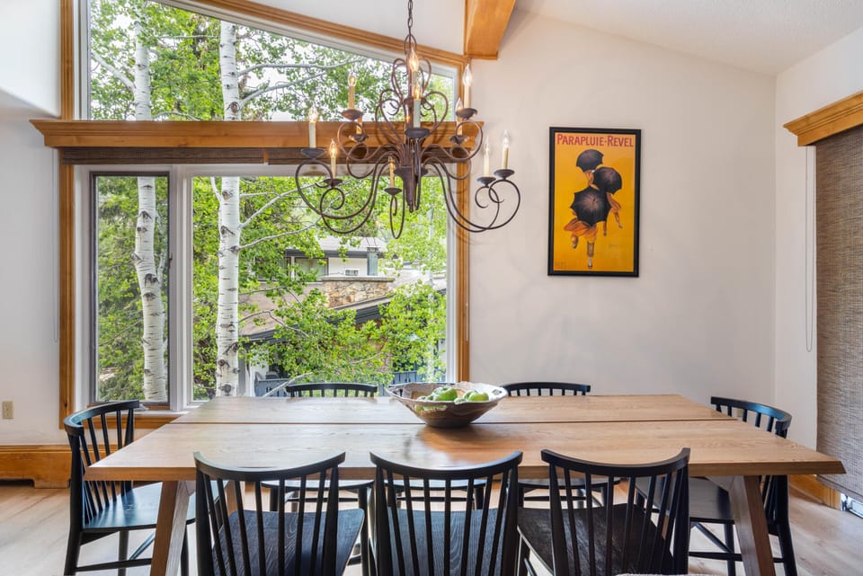 Dining room with a large wooden table surrounded by black spindle-back chairs and a wrought-iron chandelier.