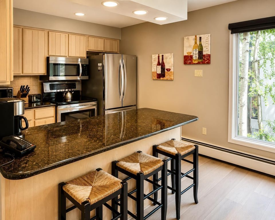 Kitchen features light wood cabinetry, stainless steel appliances, and a dark granite island with woven-seat stools.