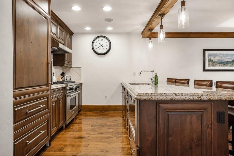 Kitchen features dark wood cabinetry, granite countertops, stainless steel appliances, and pendant lighting over the island.