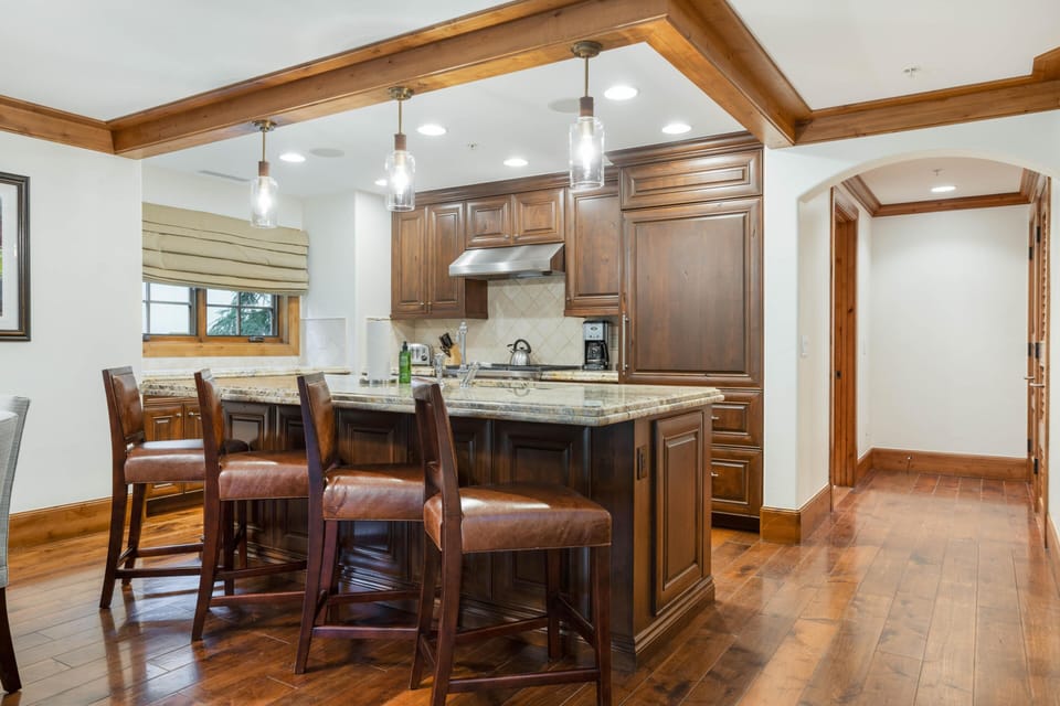 Vaulted wood beam ceiling outlines the kitchen area with recessed lighting and a window beside granite counters.
