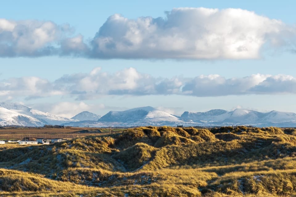 Snow-capped Snowdonia mountains viewed across the sand dunes from Lakeside, pet-friendly holiday home sleeping eight in Rhosneigr, Anglesey