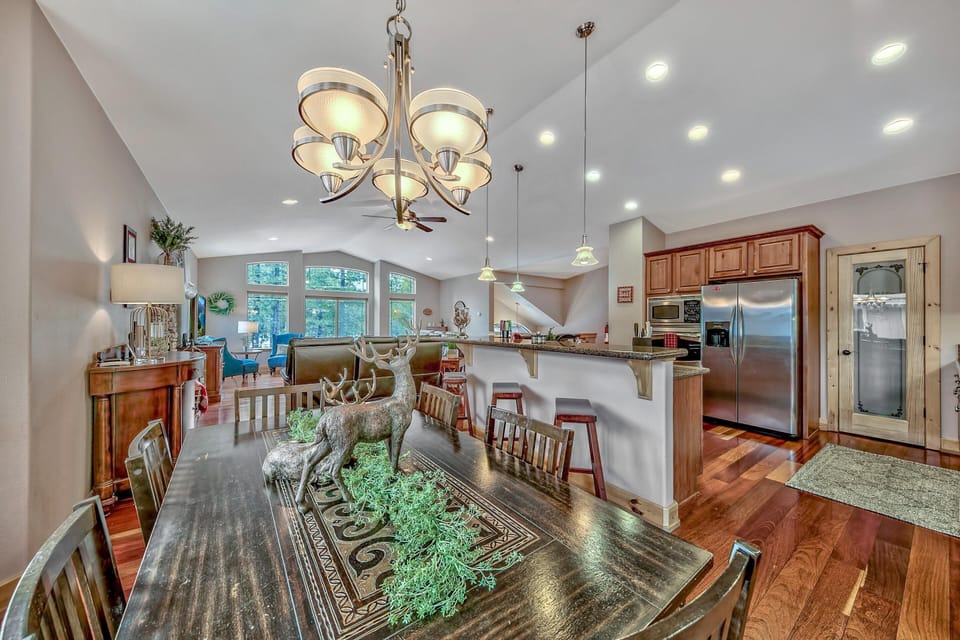 Dark wood dining table with deer centerpiece sits beside a granite breakfast bar and stainless steel kitchen appliances.