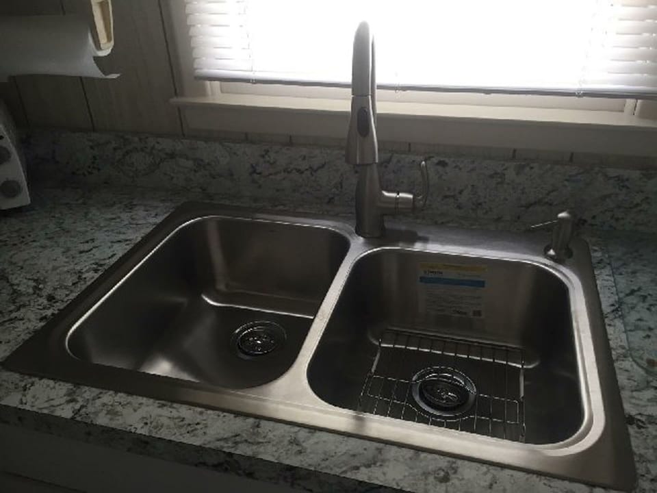 New stainless steel kitchen sink with spray hose on faucet and soap dispenser. 