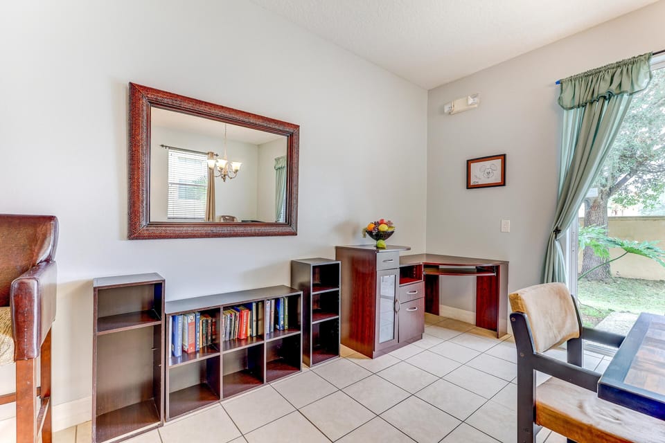 Corner desk with dark wood finish sits beside open shelving and a large framed mirror above beige tile flooring.