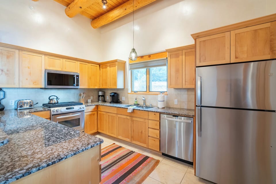 Prepare your favorite meals in this fully-equipped kitchen featuring stainless steel appliances, granite countertops, and rustic wood beam ceilings that add mountain charm.