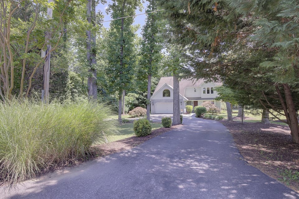 Front of house nestled amongst trees with circular driveway. 