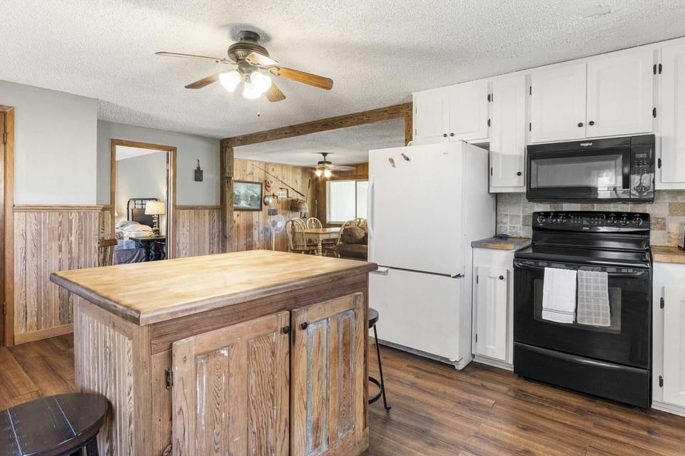 Open-concept kitchen with rustic island, black appliances, and cozy views into the dining and living areas-perfect for gathering and cooking.