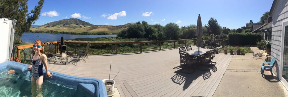 A panorama of the back deck showing the spa, patio table, and fire pit.