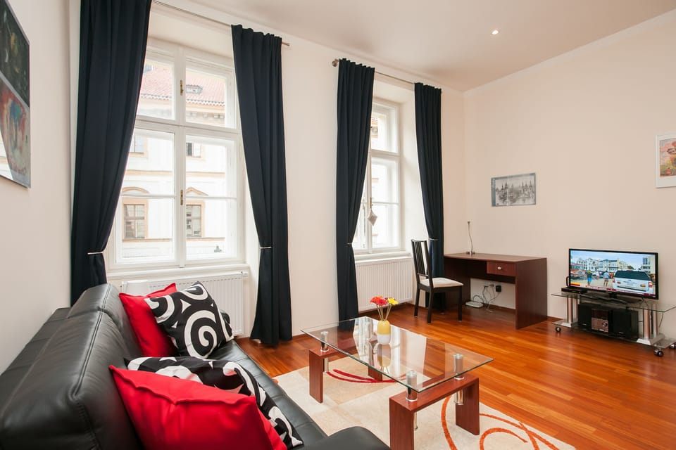 Sitting area with sofa, office desk with chair, TV, large windows, bright space