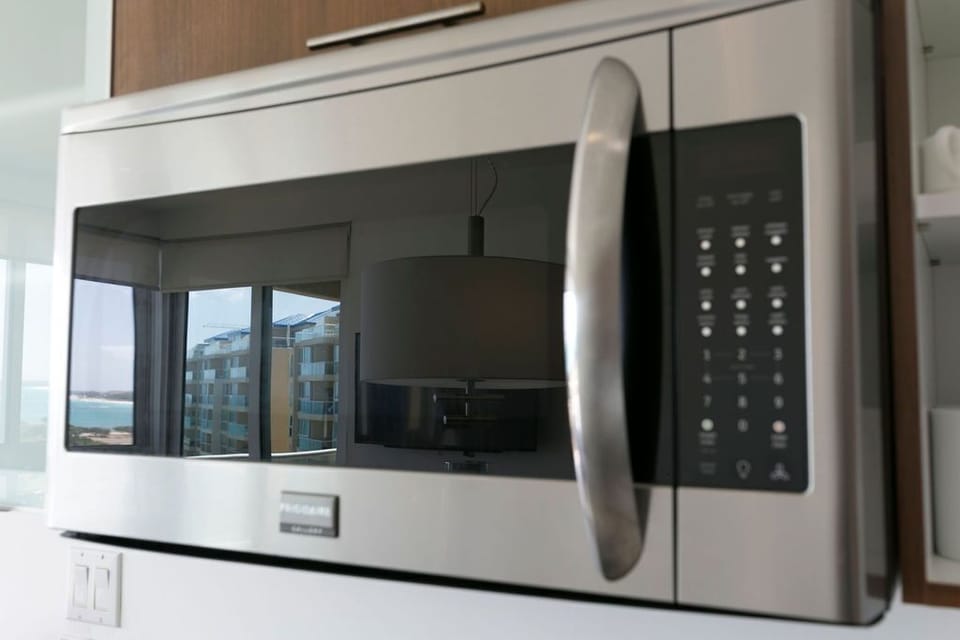 Your modern kitchen is fully equipped with essential appliances like this sleek microwave, making meal prep effortless during your stay. The waterfront views beyond invite relaxation.
