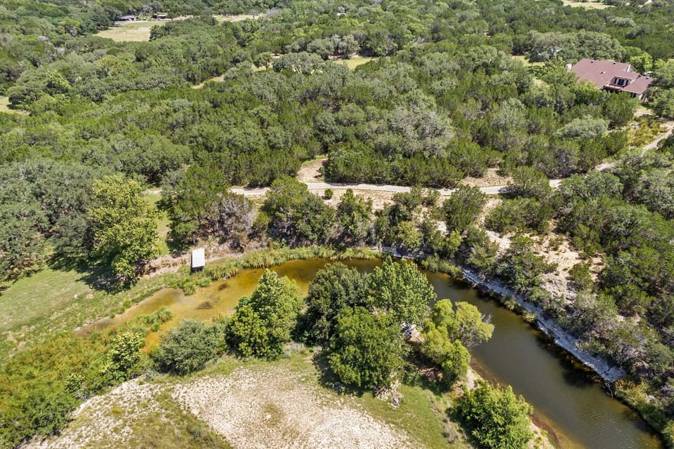 A bird's-eye view captures the serene beauty of this property, highlighting the winding creek, dense surrounding woods, and a quiet home tucked away in the landscape.