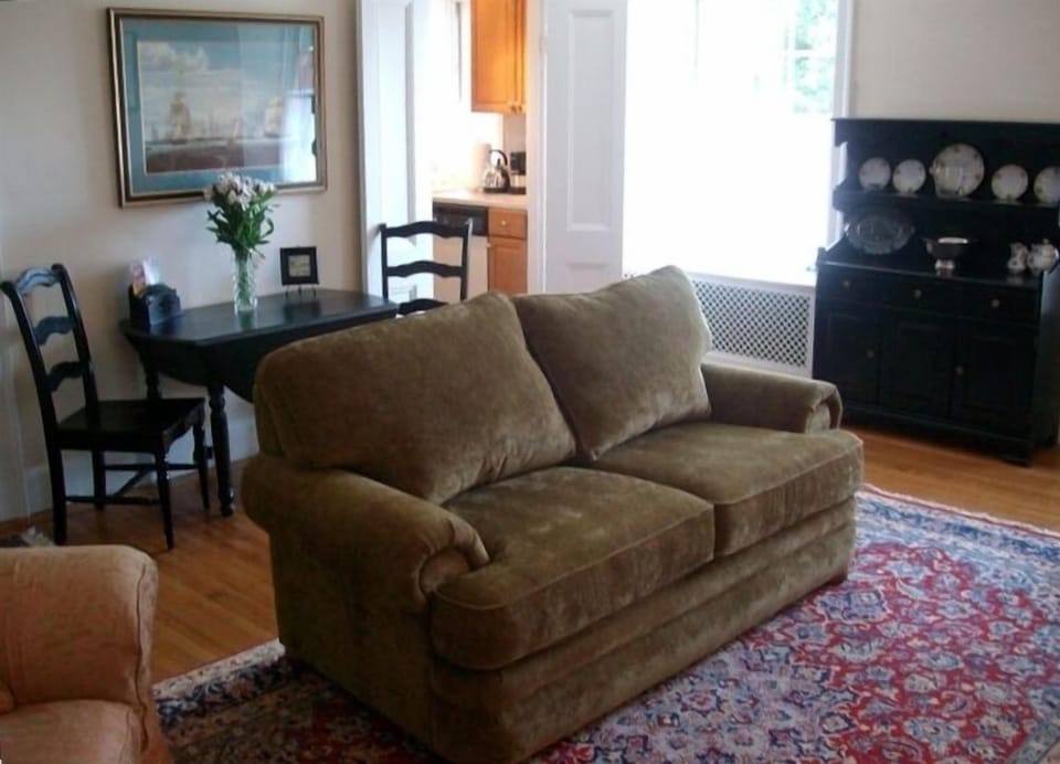 Sunny livingroom with love seat and comfy chairs, kitchen in the background.