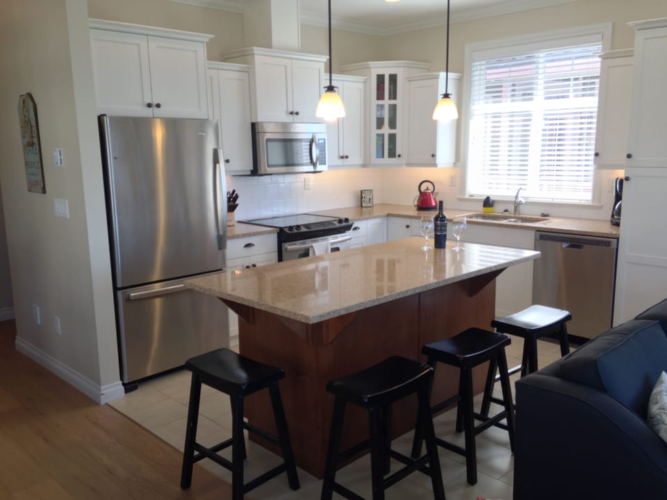 Well stocked kitchen equipped with stainless steel appliances and 4 bar stools.