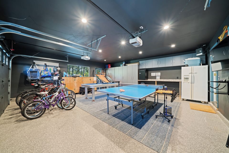 Spacious game garage with ping pong, pool table, Pop-a-Shot, and a fleet of bikes—plus extra storage and a fridge for easy, all-day hangouts.