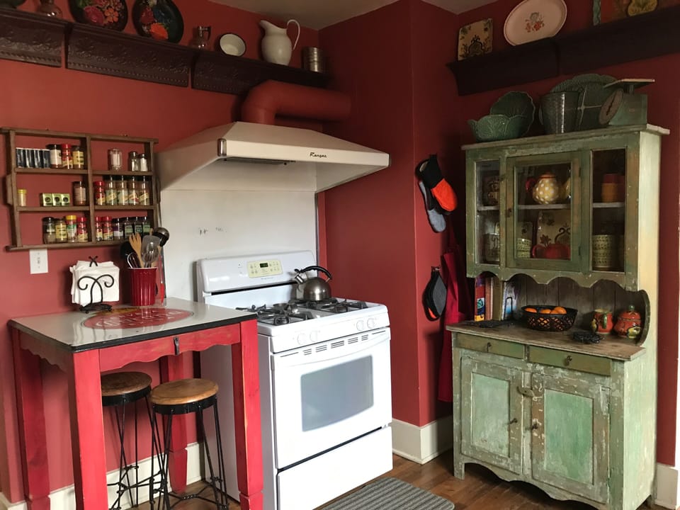 Kitchen with gas stove, spices, bright serving pieces in antique hutch.  