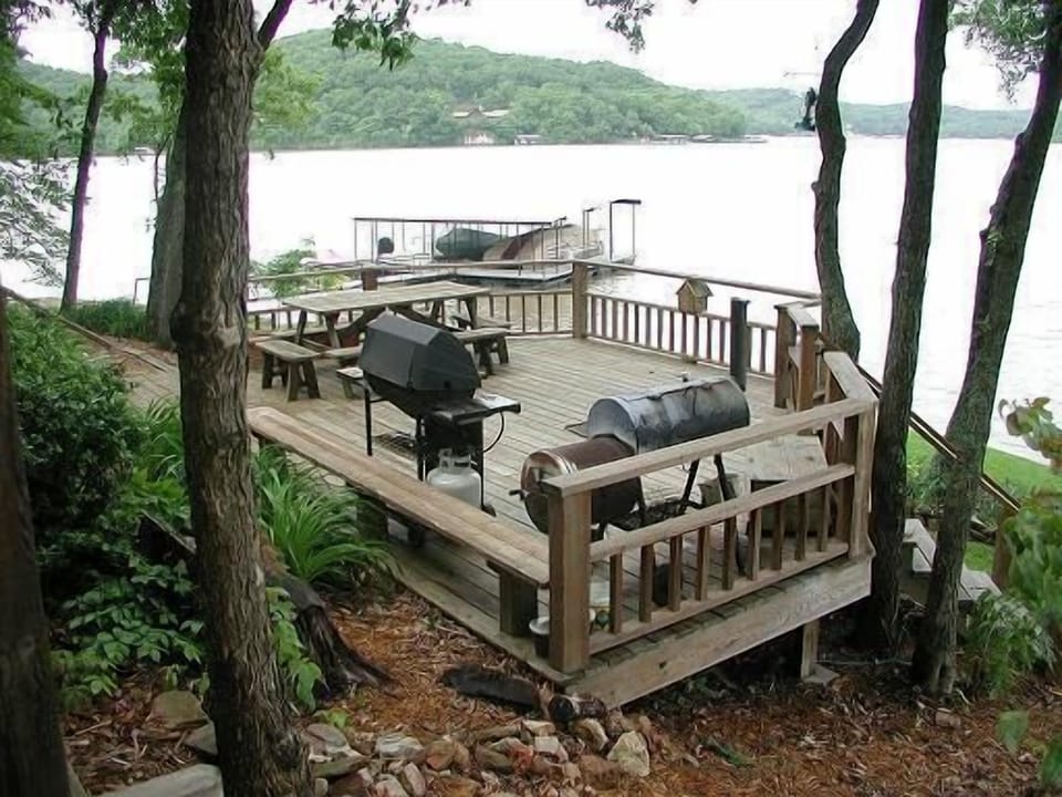 Deck is shaded by umbrella of trees with tiki lights I outdoor dining furniture