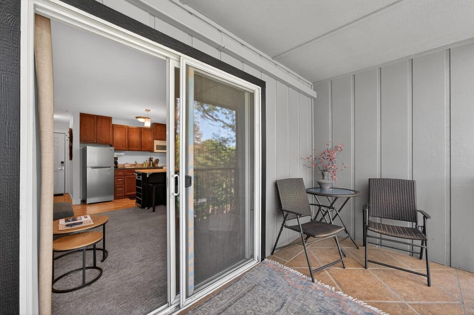 Tiled balcony with metal wicker chairs and glass-top table opens to kitchen with cherry cabinets and stainless steel fridge.